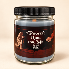 A glass jar candle with a black ribbed screw-on lid and a pirate-themed label reading 'A PIRATE'S RIDE FOR ME,' featuring a dog, a hand, and a skull-and-crossbones motif on a warm beige background.