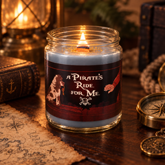 A lit candle in a clear glass jar sits on a wooden table surrounded by pirate-themed props, including a map, compass, lantern, and old book. The candle label reads “A Pirate’s Ride For Me” with an illustration of a dog and a skull-and-crossbones.