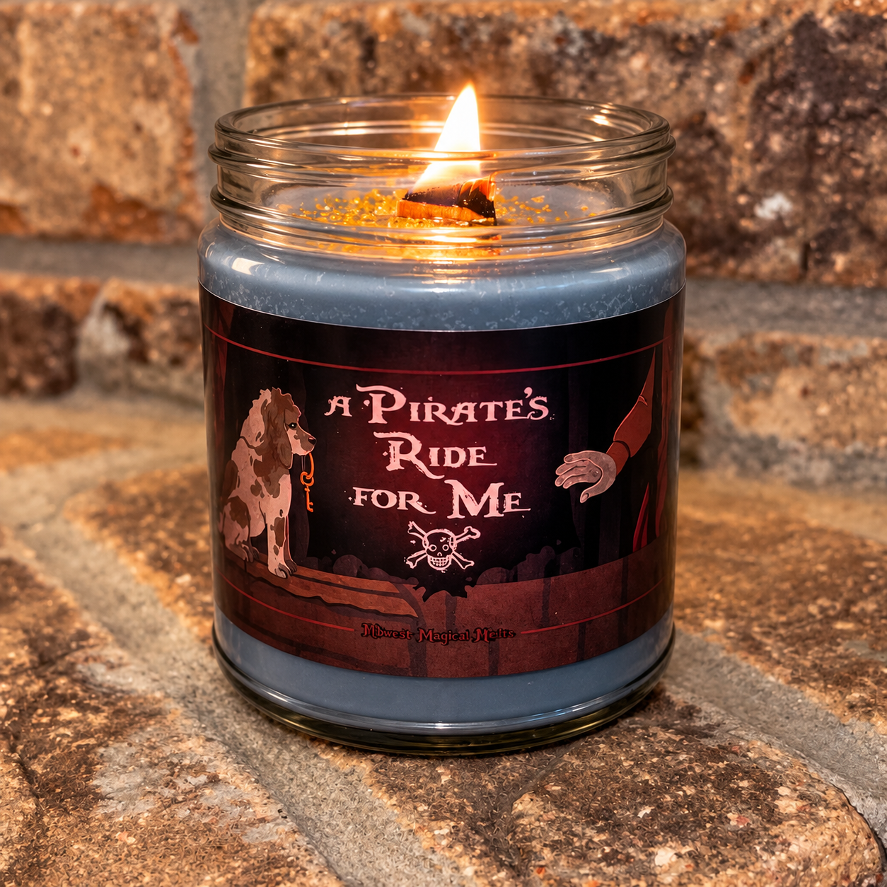 A lit blue-gray candle in a clear glass jar sits on a stone surface against a stone wall. The label reads "A Pirate's Ride for Me" with pirate-themed artwork, including a dog, a hand, and a skull-and-crossbones.