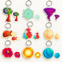A set of colorful, die-cut acrylic keychains featuring various whimsical shapes like a tree, snowflakes, a tornado, a flower, a potion bottle, and a sun, arranged on a light cream background.